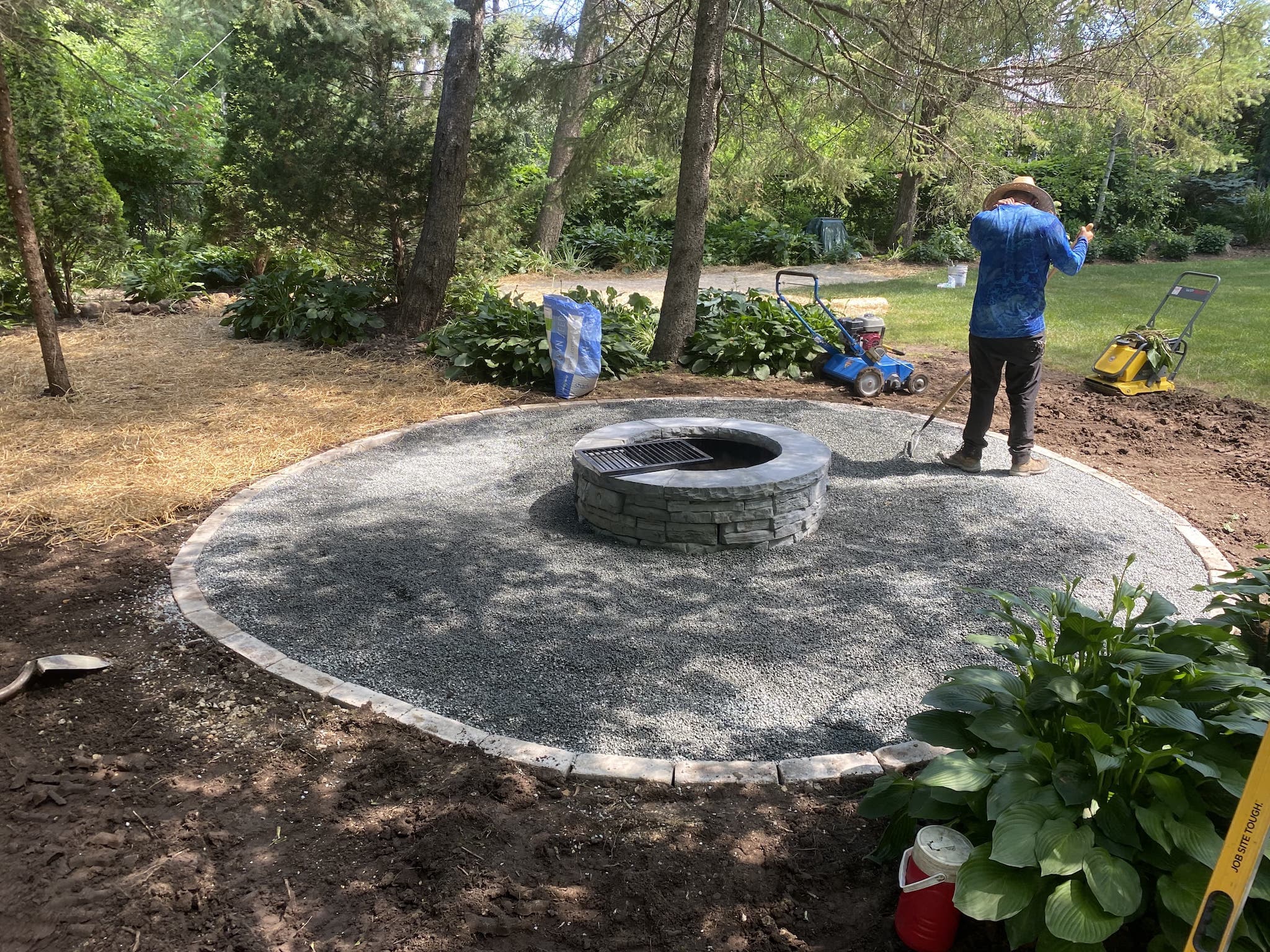 Person landscaping backyard with firepit and gravel.